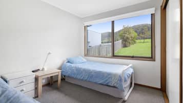 A bedroom with a single bed, a bedside table with a lamp, a dresser, and a window with a view of a green landscape.