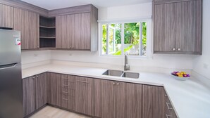 Cocina moderna con armarios de madera, refrigerador de acero inoxidable, pileta doble y ventana con vista a follaje.