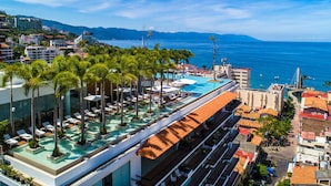 Piscina infinita no terraço, com palmeiras, espreguiçadeiras e vista para o mar.