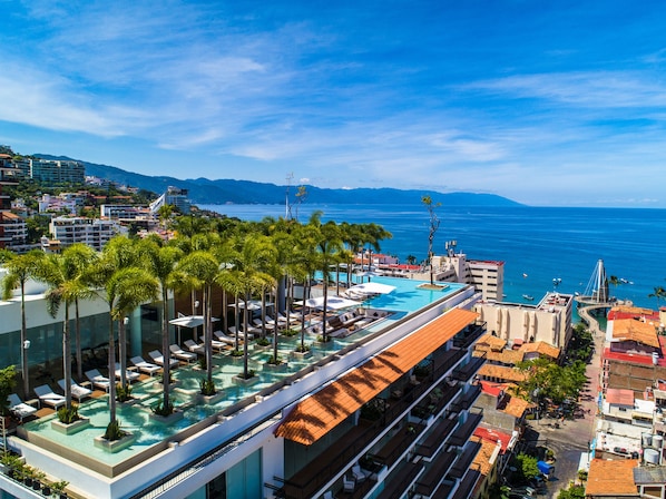 A rooftop infinity pool with palm trees, lounge chairs, and a view of the sea.