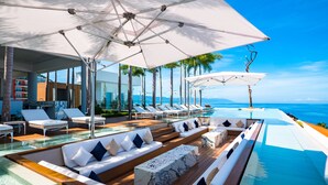 Uma área de piscina luxuosa com espreguiçadeiras, um espaço de estar e vista para o oceano.