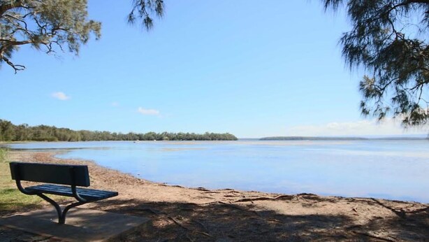 A bench by a calm lake with a clear sky.