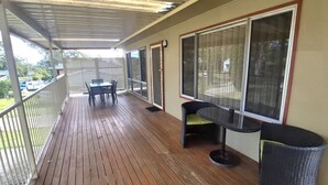 A covered outdoor area with a wooden deck, a table with chairs, and a large window.