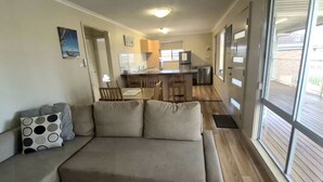 A compact living space with a sofa, dining table, kitchen area, and a sliding glass door leading to an outdoor deck.