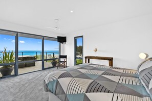 Une chambre avec un grand lit, une télévision, une chaise, une table et une vue sur l’océan.