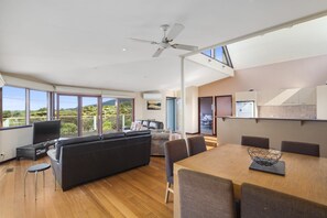A spacious living area with a large window, a ceiling fan, and a dining table with chairs. - Swingbridge (Lorne)
