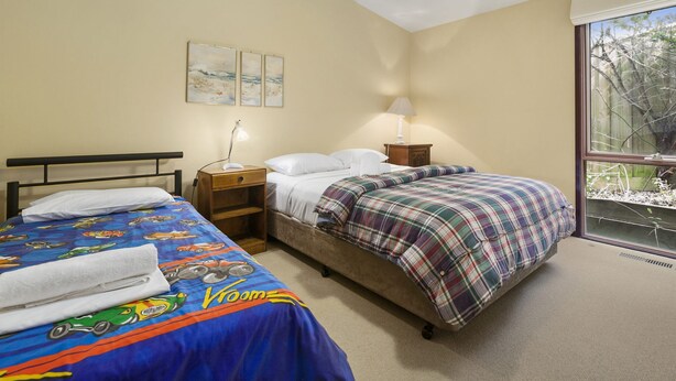 A bedroom with two beds, a nightstand, a lamp, and a window with a view of trees.