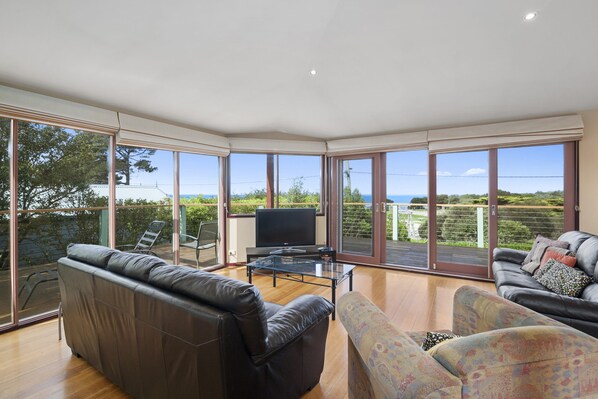 A spacious living room with a large TV, leather sofas, and a glass coffee table.