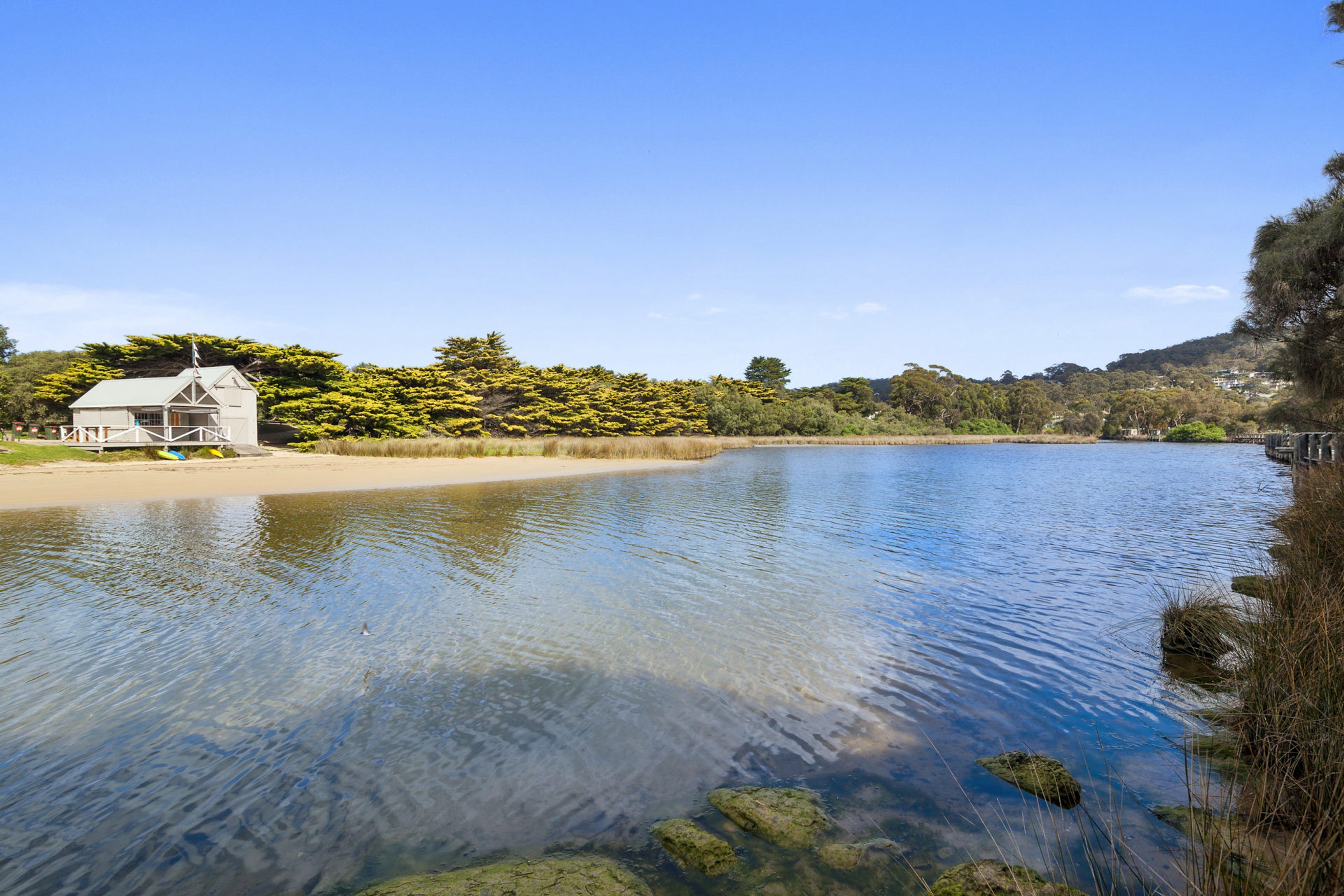 Un lac aux eaux limpides, avec un petit bâtiment sur la rive, entouré d’arbres et sous un ciel dégagé.