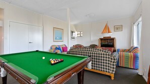 A room with a pool table, a sofa set, a television, and a window.