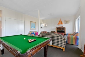 A room with a pool table, a sofa set, a television, and a window.