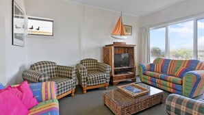 A living room with two plaid armchairs, a colorful sofa, a wooden TV stand, and a wicker coffee table.