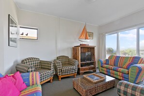 A living room with two plaid armchairs, a colorful sofa, a wooden TV stand, and a wicker coffee table.