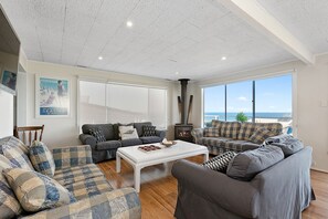 A living room with a fireplace, large windows, and a view of the sea.
