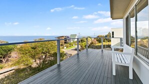 A wooden deck with a white bench, overlooking a coastal landscape with a clear sky.