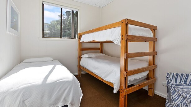 A room with a bunk bed and a single bed, a window with a view of trees, and a framed picture on the wall.