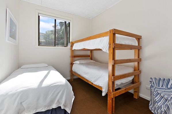 A room with a bunk bed and a single bed, a window with a view of trees, and a framed picture on the wall.