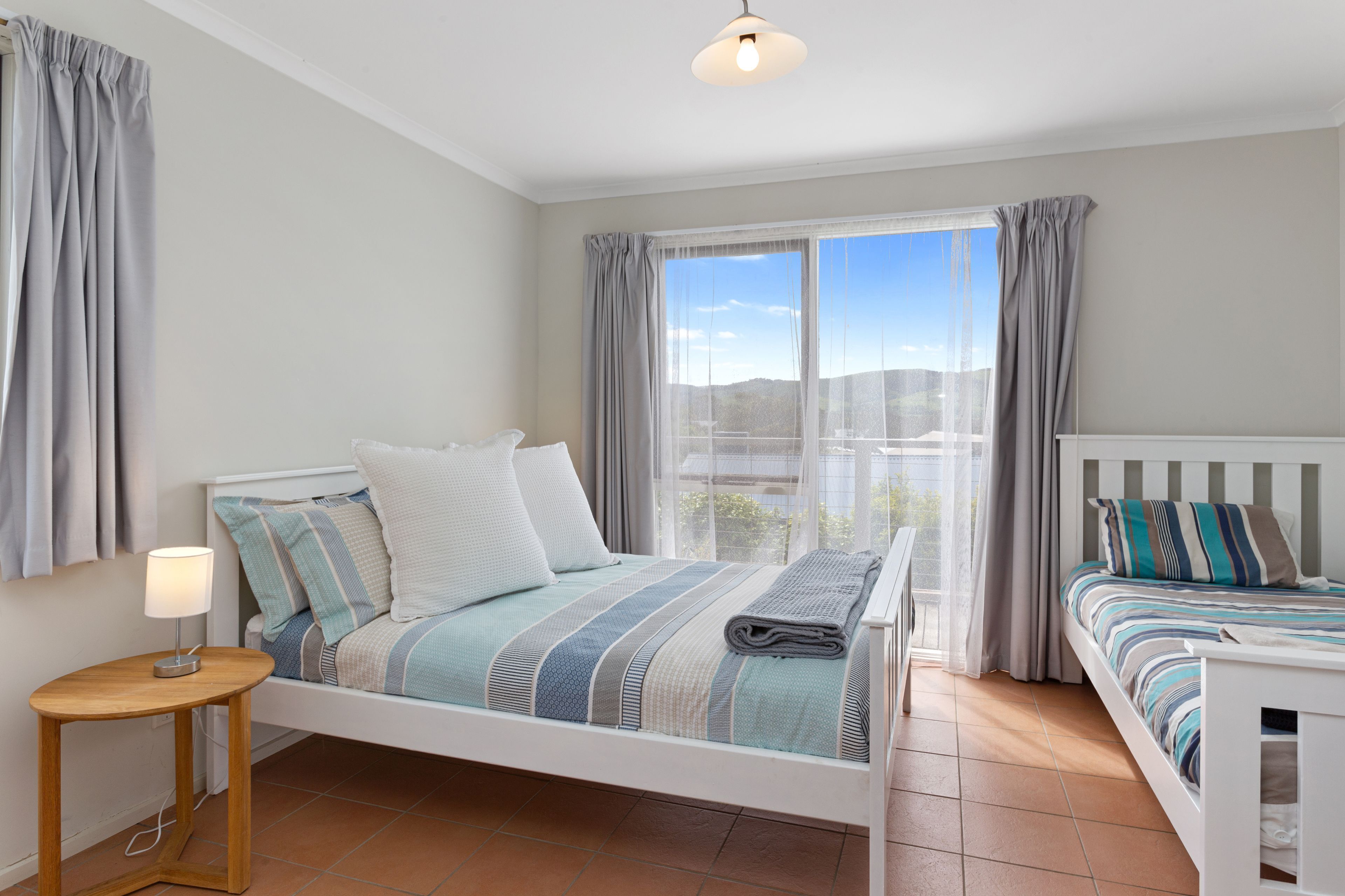 A bedroom with a bed, bedside table, lamp, and a view of the outdoors.