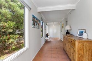 Un pasillo con vistas a un jardín, un cuadro, una lámpara y un tablero de ajedrez.
