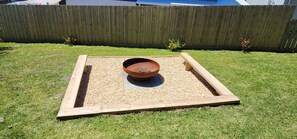 A square wooden structure with a metal bowl in the center, surrounded by gravel, set on a grassy lawn. - Coleridge (Marengo)