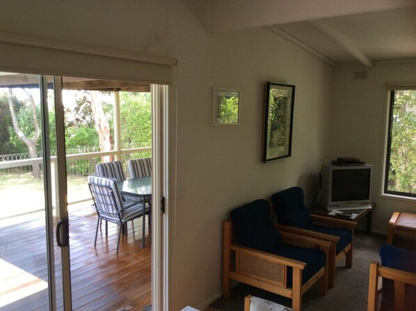 A room with a sliding glass door leading to an outdoor deck, a television on a stand, and two sofas.