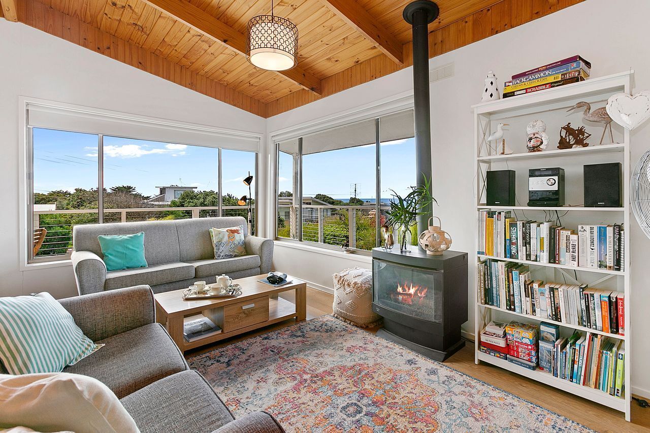 A spacious living room with a fireplace, a bookshelf, and large windows offering a view of the outdoors.