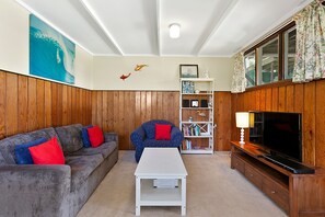 A living room with a grey sofa, a blue armchair, a white coffee table, a bookshelf, and a television. - Surf Reef (Marengo)