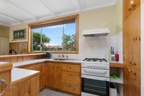 A kitchen with wooden cabinets, a gas stove, a sink, and a window with a view of trees.