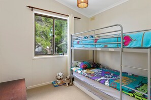 Ein Stockbett mit farbenfroher Bettwäsche, ein Fenster mit Vorhängen und ein kleiner Tisch mit einem Fußball und Gesellschaftsspielen.