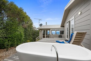 A house with a patio area featuring a hot tub, a deck, and a view of the ocean.