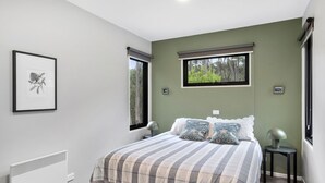 A bedroom with a bed, two bedside tables, a radiator, and two windows with blinds.