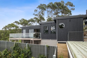 A modern two-story house with a balcony, large windows, and a wooden deck. - Summer By The Bay (Lorne)