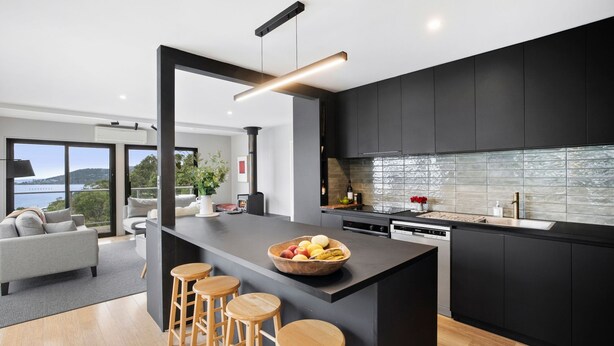 A modern kitchen with a central island, bar stools, and a view of the outdoors.