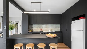 A modern kitchen with a central island, bar stools, dark cabinetry, and a white refrigerator.