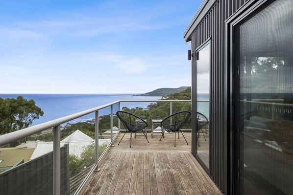 A balcony with a view of the sea, two chairs, and a glass door.
