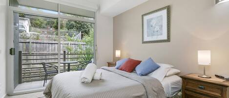 Una camera da letto con un letto, comodini, un quadro incorniciato e vista su uno spazio esterno tramite una porta vetrata.