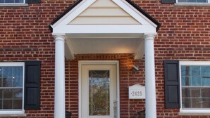 A brick building with a white front door, a small porch, and a mailbox with the number 2425. - The House of CROY (Alexandria)