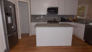 A modern kitchen with white cabinetry, a granite countertop island, stainless steel appliances, and a backsplash with gray tiles. - The House of CROY (Alexandria)