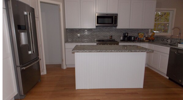 A modern kitchen with white cabinetry, a granite countertop island, stainless steel appliances, and a backsplash with gray tiles. - The House of CROY (Alexandria)