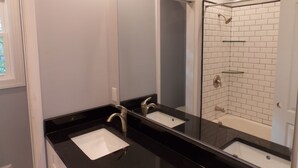 A bathroom with two sinks, a large mirror, and a shower area with white tiles. - The House of CROY (Alexandria)