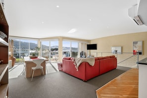 A modern living room with a red sofa, a dining area with a white table, and large windows offering a view of the outdoors.