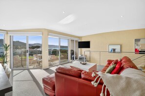A modern living room with a red leather sofa, a flat-screen TV mounted on the wall, and a large sliding glass door leading to an outdoor patio.