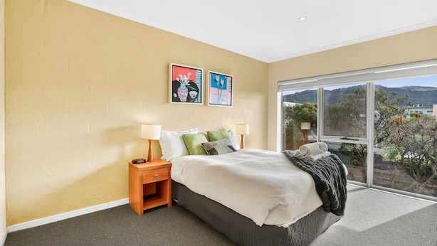 A bedroom with a large window, a bed with pillows, a nightstand, and two wall art pieces.