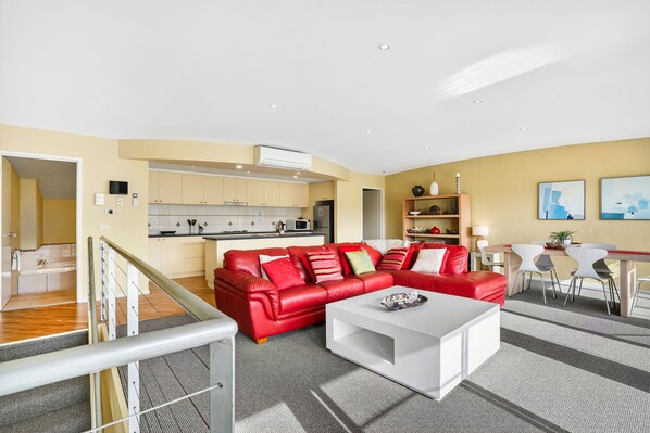 A modern living room with a red leather sofa, a white coffee table, and a kitchen in the background.