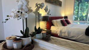 Ein Schlafzimmer mit einem Bett, Kissen, einem Nachttisch, einer Lampe und einem Spiegel, der den Raum reflektiert.