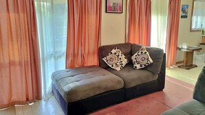 Un salon avec un canapé, deux coussins à motifs, un tableau encadré au mur et une fenêtre avec des rideaux.