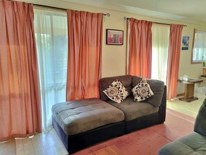 A living room with a sofa, two patterned cushions, a framed picture on the wall, and a window with curtains.