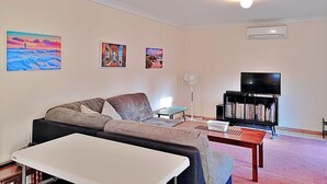 Un salon comprenant un canapé, une table basse, un meuble pour la télévision avec un téléviseur à écran plat et un ventilateur de plafond.