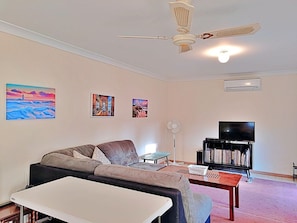 A living room with a sofa, a coffee table, a TV stand with a flat-screen TV, and a ceiling fan.