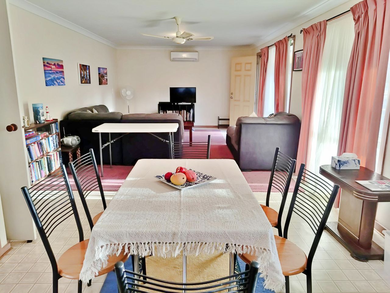 A dining area with a table set for four, a sofa, a television, and a bookshelf.